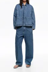 Chaqueta corta de denim en color azul con diseño de rayas verticales blancas, cuello camisero, bolsillos delanteros de parche y cierre frontal con botones metálicos.
