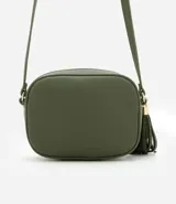 Cartera bandolera pequeña color beige, confeccionada en poliuretano con textura granulada. Presenta cierre superior con cremallera, correa larga ajustable y detalle de borla decorativa en el lateral con herrajes dorados.