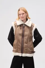 Chaleco negro de efecto cuero con forro y cuello de corderito. Presenta cierre frontal de cremallera, bolsillos laterales y diseño sin mangas.