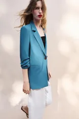 Blazer negro de cuello con solapas de muesca y hombreras, con mangas tres cuartos drapeadas, bolsillos de vivo simulados y cierre frontal con un botón dorado. Forro interior a tono.