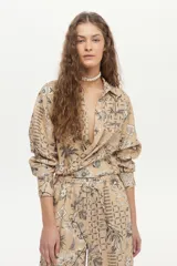Camisa beige de manga larga, con cuello camisero, cierre frontal con botones y un estampado detallado de motivos botánicos e insectos en tonos oscuros.