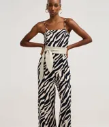Mono largo de sastrería marca Cortelle, confeccionado en crepé con elastano, con estampado animal print de cebra en tonos beige y negro. Presenta escote recto, tirantes finos regulables, corte wide leg en las piernas y un cinturón ancho ajustable en la cintura.