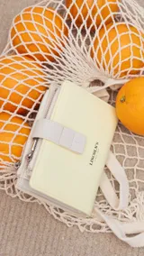 Billetera mediana de diseño compacto, color amarillo pastel con detalles en blanco. Cuenta con cierre de presilla, compartimento principal con cierre metálico y logo de la marca grabado en el frente.