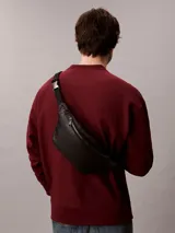 Riñonera Calvin Klein negra de poliuretano, diseño waist bag con cierre de cremallera superior, correa ajustable y monograma CK grabado en la parte delantera.