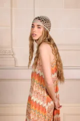 Vestido largo tipo solera con diseño plisado y estampado geométrico en zigzag en tonos naranja, crema y gris. Presenta breteles finos y una silueta holgada y fluida.