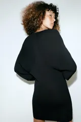 Vestido corto de punto negro confeccionado en mezcla de viscosa, con cuello barco, manga larga y detalle de costuras marcadas.