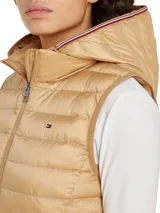 Chaleco acolchado color beige con capucha desmontable, cierre frontal con cremallera, dos bolsillos laterales con cremallera y logo de Tommy Hilfiger bordado en el pecho. Confeccionado en poliéster reciclado con acabado repelente al agua.