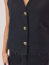 Chaleco negro sin mangas, de corte recto y largo a la cintura, con cuello redondo y cierre frontal oculto.