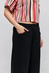 Babucha de calce relajado color negro, con cintura elastizada, cordón de ajuste y bolsillos laterales. Presenta un diseño de pernera amplia y cómoda.