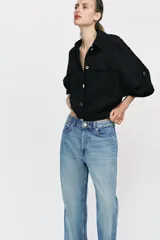 Blusa negra de cuello solapa y manga corta, con bolsillos con solapa en el pecho, bajo elástico y cierre frontal con botones.