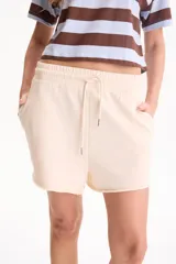 Short deportivo sin friza color beige, con cintura elástica con cordón ajustable, bolsillos laterales y terminaciones deshilachadas.