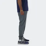 Pantalón jogger deportivo New Balance, color gris oscuro, confeccionado en tejido de poliéster reciclado con tecnología NB DRY. Presenta cintura elástica con cordón de ajuste interno, dos bolsillos laterales y puños elásticos en los tobillos.