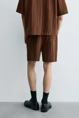 Bermuda de corte relajado color marrón con finas rayas verticales negras. Presenta cintura elástica ajustable con cordón y bolsillos laterales y trasero.