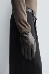 Guantes de cuero negro con interior forrado en tejido de punto. Presentan costuras decorativas en el dorso y tecnología táctil en los dedos para el uso de dispositivos móviles.