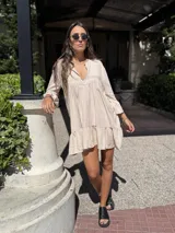 Vestido corto color beige de fibrana, con escote en V, mangas 3/4 con volados y falda con volados.