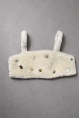 Top corto de corderito natural con breteles anchos, decorado con diversos pins metálicos y botones decorativos en el frente. Cuenta con cierre de broches en la espalda.