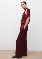Pantalón wide leg de tiro medio en tejido satinado color bordó, con pinzas delanteras, trabillas, bolsillos laterales y cierre oculto con botón, gancho y cremallera.