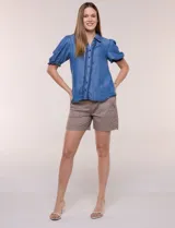Camisa de lyocell color azul con efecto denim, cuello camisero, cierre frontal con botones y detalles de bordado oscuro a lo largo de la botonera. Presenta mangas cortas abullonadas con puños elásticos y terminación con volados.