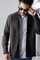 Camisa verde militar de corte recto, con cuello clásico, cierre frontal con botones a presión, mangas largas con puños abotonados, dos bolsillos de parche en el pecho y bajo redondeado.