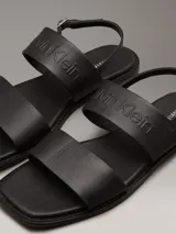 Sandalias planas Calvin Klein de cuero sintético negro, con puntera cuadrada, doble tira ancha y correa ajustable en el tobillo.