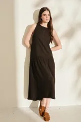Vestido midi negro sin mangas, con cuello redondo, corte recto en la parte superior y falda amplia con vuelo. Presenta costuras decorativas verticales y un detalle deshilachado en el dobladillo inferior.