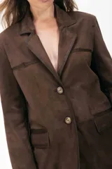 Blazer de ante color marrón con silueta oversize, cierre frontal con botones, bolsillos con solapa y tajo trasero. Presenta detalles de costuras con terminaciones pintadas a mano.