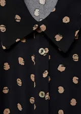 Vestido largo de estilo camisero confeccionado en viscosa, con estampado de lunares en contraste. Presenta cuello camisero, cierre frontal de botones, mangas largas con puños abotonados y un detalle de nudo ajustable en la cintura que define la silueta.