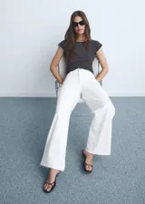 Jeans blancos de tiro alto con diseño acampanado y bajo deshilachado, con cierre de cremallera y botón, trabillas para cinturón y bolsillos traseros.