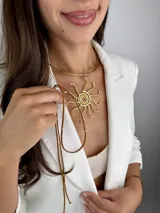 Colgante de diseño en latón dorado, compuesto por una gargantilla rígida circular y un dije central en forma de sol con líneas orgánicas. Incluye un cordón de cuero marrón ajustable con detalles metálicos.