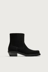 Bota estilo cowboy fabricada en piel con acabado serraje y parte superior lisa. Cuenta con horma cuadrada, cierre mediante cremallera lateral y suela con ligero tacón.
