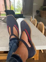 Ballerinas de gamuza color marrón oscuro con diseño tipo T-strap y detalles de costuras decorativas en color verde oliva. Cuentan con cierre de pulsera al tobillo y suela plana.