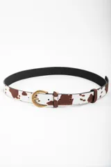 Cinto con estampado de vaca en tonos marrones y blancos, con hebilla metálica dorada envejecida.