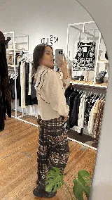 Blusa de lino color beige con cuello alto y volados en el frente y mangas. Presenta detalles de ribetes en terciopelo negro que contrastan con la tela principal. Posee mangas largas con puños abotonados y un diseño romántico y femenino.