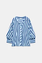 Camisa de rayas verticales azules y celestes, con cuello solapa, escote en V, cierre frontal con botones y mangas largas abullonadas con puños ajustados.