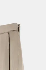 Pantalón bombacho de tiro medio en hilatura de viscosa color beige, con bolsillos laterales ocultos, volantes delanteros a tono, bajo abullonado con elástico y cierre lateral con cremallera oculta.