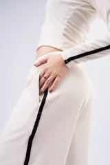 Pantalón tipo palazzo de tejido acanalado en color crema, con corte amplio y fluido. Presenta una franja lateral negra a lo largo de la pierna y bolsillos laterales.