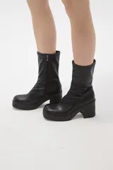 Bota de caña media en cuero sintético color negro, con plataforma y taco cuadrado. Presenta costura central en el empeine y cierre lateral interno.