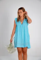 Vestido corto color celeste de tela calada con cuello en V y mangas cortas con volado. El ruedo tiene un borde festoneado.