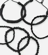 Set de seis pulseras de estilo casual, todas en color negro. Incluye tres pulseras trenzadas ajustables con cordón y tres pulseras con cuentas elásticas (algunas de cuentas lisas y otras de cuentas texturizadas).