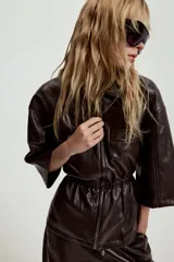 Chaqueta de efecto piel con cuello solapa, manga corta y cintura elástica. Presenta cierre frontal con cremallera y bolsillos decorativos en el frente.