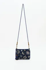 Cartera tipo sobre de algodón azul marino con bordados de motivos celestiales como lunas y estrellas en tonos dorados y plateados. Incluye una correa larga trenzada, cierre superior con cremallera y un detalle de borla decorativa en el lateral.