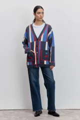 Cardigan de punto con diseño de bloques de color en azul, rojo y beige. Presenta cuello en V, cierre frontal con botones y dos bolsillos delanteros con bordado de cerezas.