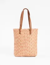 Bolso tipo canasto de playa con diseño tejido en tonos naranja y blanco. Tiene doble asa de cuero marrón.