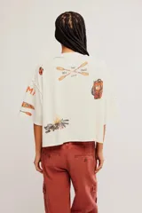 Remera de algodón liviano color blanco marfil con estampa de inspiración campestre, calce recto, estilo oversize, largo corto, escote redondo, hombros caídos y mangas cortas.