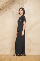 Conjunto de dos piezas compuesto por una blusa de corte holgado con detalle de flor aplicada en el pecho y un pantalón de corte recto y tiro alto, ambos en color negro y confeccionados en tela con textura.