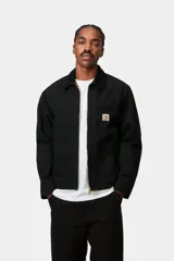 Campera Detroit de Carhartt WIP color negro, confeccionada en resistente lona de algodón con cuello de pana al tono. Cuenta con cierre frontal metálico, bolsillos frontales ribeteados y un bolsillo en el pecho con cierre de cremallera y etiqueta distintiva de la marca.