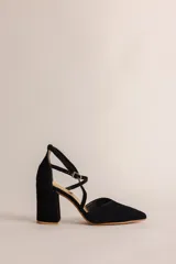 Zapato de tacón negro de gamuza con punta fina, escote en V y tiras cruzadas en el tobillo con hebilla. El tacón es de 8 cm.