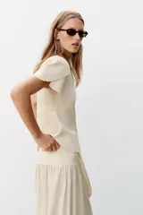 Chaqueta entallada azul marino de punto, con cuello redondo y mangas cortas abullonadas con aberturas. Cierre frontal con botones forrados a tono.