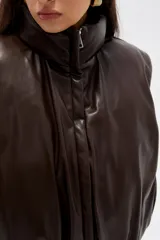 Chaleco acolchado de cuero sintético en color marrón oscuro, con cuello alto, cierre frontal y diseño holgado.