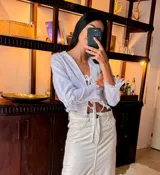 Camisa blanca de lino con escote en V, mangas largas con puños fruncidos y cierre frontal con lazos.